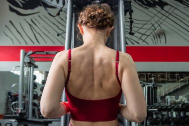 Sporcu genç bir kadın spor salonundaki bir makinede onu eğitmek için egzersiz yapıyor..