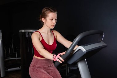 Spor kıyafetli genç bir kadın spor salonunda egzersiz bisikleti kullanıyor..