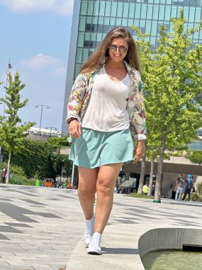 Açık hava kentsel arka planında rahatça yürüyen orta büyüklükte genç bir kadın..