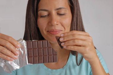 Happy woman break to eat dark chocolate bar at home. clipart