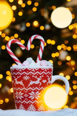 Noel kartpostalında zencefilli kurabiye, Noel süslü kırmızı kupa Noel ağacı süsleri ve kırmızı çizgili bayram şekerleri. Arkaplanda marşmelov olan Xmas şekeri ve fincanı