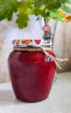 Jar of jam on the table. May be strawberry or dogwood confiture in glass jar. Green leaves in the background. Homemade preparations and canning. Selective fokus.