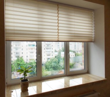 Pleated blinds XL, beige color, with 50mm fold closeup in the window opening in the interior. Home blinds - modern bottom up privacy shades half raised on apartment windows. 