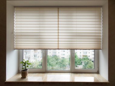 Pleated blinds XL, beige color, with 50mm fold closeup in the window opening in the interior. Home blinds - modern bottom up privacy shades half raised on apartment windows.  clipart