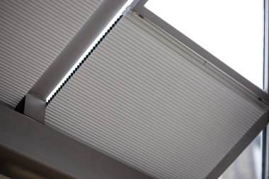 Motorized pleated blinds on the roof windows. Blinds for skylights, beige color. Honeycomb pleated blinds on glass roof. clipart