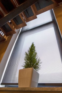 Merdivenin altındaki pencerede paten kör. Evin mahremiyeti için paten perdesi kumaşı. Pencere pervazında bir çiçek var..