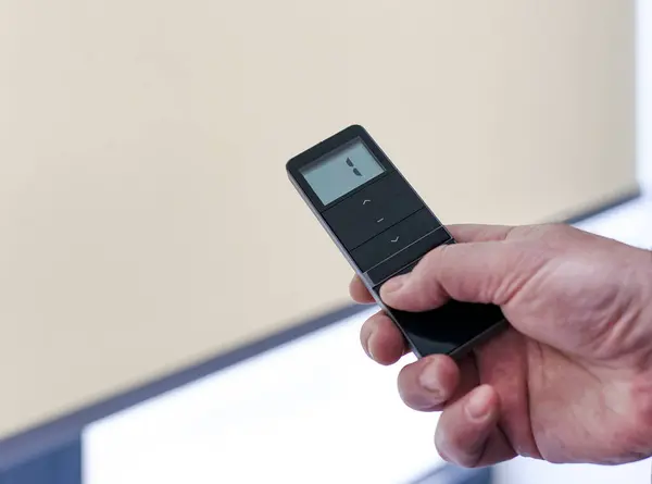 Pencere perdeleri için uzaktan kumanda. Adam elinde siyah uzaktan kumanda paneli tutuyor ve motorlu paten perdelerini çalıştırıyor. Radyo kontrol panjurları yakın plan..