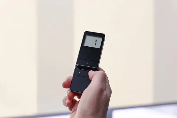 Pencere perdeleri için uzaktan kumanda. Adam elinde siyah uzaktan kumanda paneli tutuyor ve motorlu paten perdelerini çalıştırıyor. Radyo kontrol panjurları yakın plan..