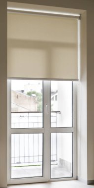 Bej jaluzi, balkona açılan büyük cam kapıyı kapatmak için aşağı çekiliyor. Kapı beyaz süslemeyle çerçevelenmiş ve duvar soluk bej renkte..