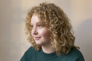 Gülümseyen sarışın genç kadın. Kıvırcık kıvırcık, kızıl saçlı, hayalperest kız. Stüdyoda portre. Doğal ışık pencereden içeri süzülüyor. Pastel arkaplan.