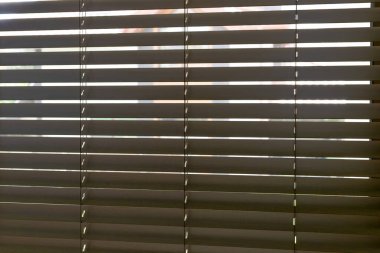 Yatay ahşap yakın plan. Çatalların arasından süzülen doğal ışık, çizgili ışık ve gölge deseni yaratıyor. Bulanık açık hava ayrıntıları belli belirsiz görünür, derinlik ve sakinlik ekler.