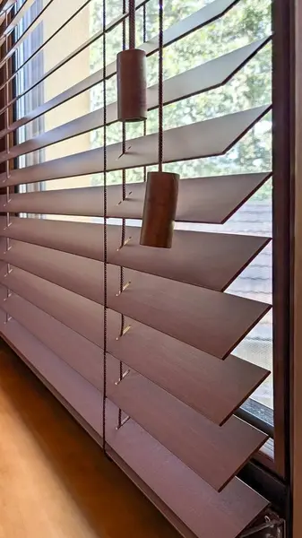 Yatay çıtçıtlarla ahşap panjurlar ve çekme kabloları, dışarıda yumuşak doğal ışık ve yeşil yaprakları açığa çıkarmak için kısmen açık. Ahşap panjurların tasarımı işlevselliği tarzla birleştirir, gizlilik sunar.