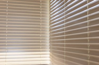 Bej rengi ahşap panjurlar, yakın çekim görüntü, pencereyi kaplayan yumuşak güneş ışığı, levhaların arasından süzülüyor 50 mm. Tahta panjurlar, iç uzaya sıcaklık ve doku ekleyerek bir ışık ve gölge deseni oluşturur..