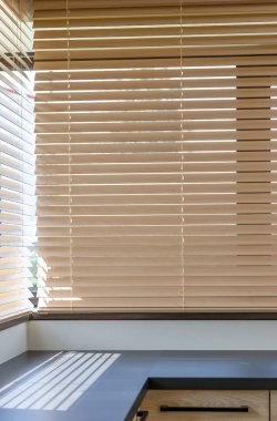 Güneş ışığı mutfakta kısmen açık bej rengi jaluzilerden geçiyor. Işınlar modern karanlık bir masa boyunca çizgili gölgeler yaratıyor. Parlak bir köşedeki mutfak çalışma alanında. Pencerelerinde tahta panjurlar var..