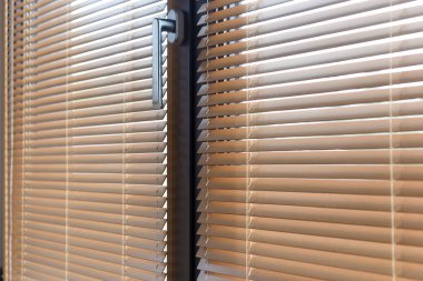 Ahşabın detaylı bir görüntüsü yakından kör eder. 25 mm çıtçıtlı Venedik panjurları alüminyum pencere kuşaklarına monte edilir. Perdelerin kablo sabitlemesi. Parlak bir metal sapı sıcak tonlara zıt düşer..