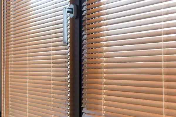 Ahşabın detaylı bir görüntüsü yakından kör eder. 25 mm çıtçıtlı Venedik panjurları alüminyum pencere kuşaklarına monte edilir. Perdelerin kablo sabitlemesi. Parlak bir metal sapı sıcak tonlara zıt düşer..