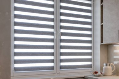 Mutfağın iç tarafındaki pencereye çift silindirli jaluziler yakın çekim. Gri renkte çift tekerlekli paten. Zebra kör olur. Işık kontrolü ve modern pencere tedavisi için gece gündüz ikili sistem.