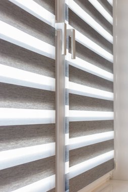 Penceredeki çift silindirli panjurlara yakın çekim. Bu zebra panjurları modern yaşam alanları için ideal, katman ve opak kumaş katmanları arasında dönüşümlü olarak çok yönlü ışık kontrolü ve mahremiyet sunar..