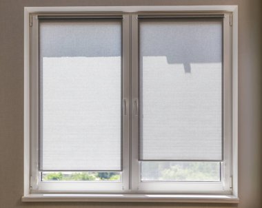 Güneşli bir günde, odanın penceresinde yakın plan gri perdeler. Pencere kuşaklarında küçük perdeler var. Koyu renk kumaşlı güneş kremi..