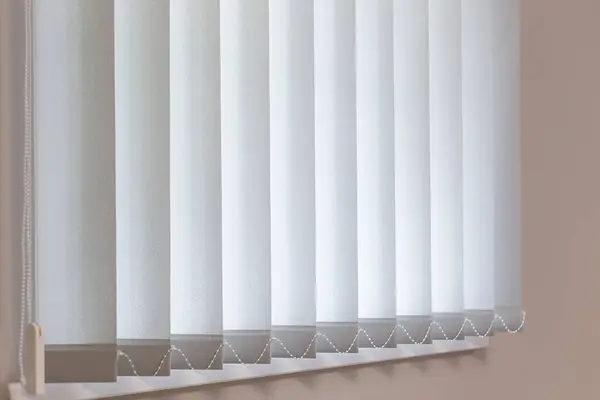 Dikey perdeler kısmen açık, yumuşak ışığın rahat bir iç kısma süzülmesine olanak sağlıyor. Panjurlar davetkar bir ortam yaratıyor. Gündüzleri odada sakin bir ortam yaratıyor..