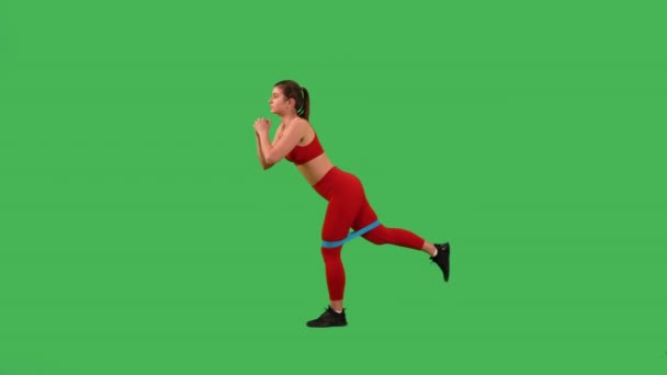 強い足のための抵抗バンドと運動をするスポーティーな女性は 赤の上とスポーツのレギンスを身に着けていますグリーンスクリーンスタジオに隔離 — ストック動画