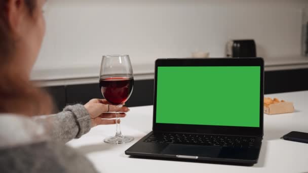 厨房里 一个晚上 女人在桌上放着绿色屏幕的展示笔记本电脑 一边喝着红酒 一边看着笔记本电脑 — 图库视频影像