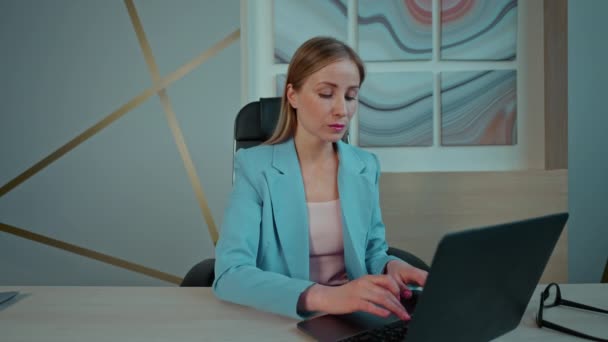 オフィスでノートパソコンを使ってエレガントなブルーのジャケットを着た女性がデスク仕上げのプロジェクトに座り — ストック動画