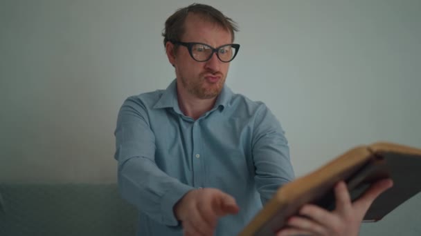 Hombre Divertido Lleva Gafas Hojas Través Libro Hace Caras Interior — Vídeos de Stock