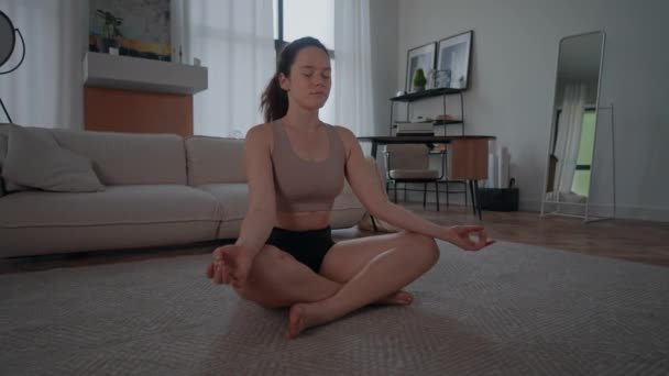 スポーツウェアを着て床に座っている女性幸せな朝ヨガの練習自宅でストレスを軽減するため — ストック動画