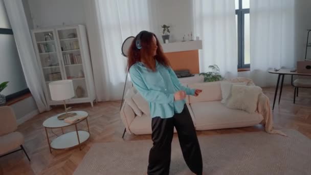 活跃的女性在客厅里跳舞 在家用耳机听音乐 — 图库视频影像