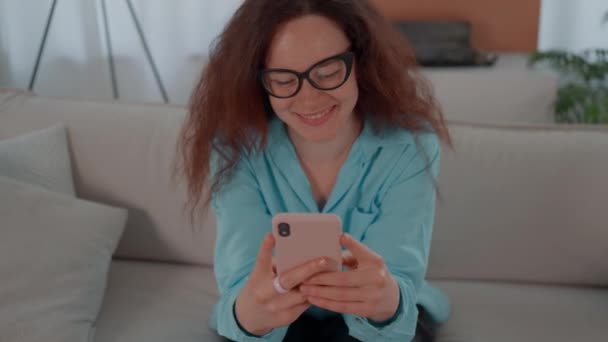 一个女人坐在沙发上 凝视着面前的手机屏幕 她专注于设备 浏览或发短信 免版税图库视频片段