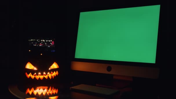 在黑暗的房间里 桌子上的南瓜中间 陈列着一台绿色屏幕的电脑 屏幕可以在黑暗的背景下编辑或显示任何想要的内容 免版税图库视频