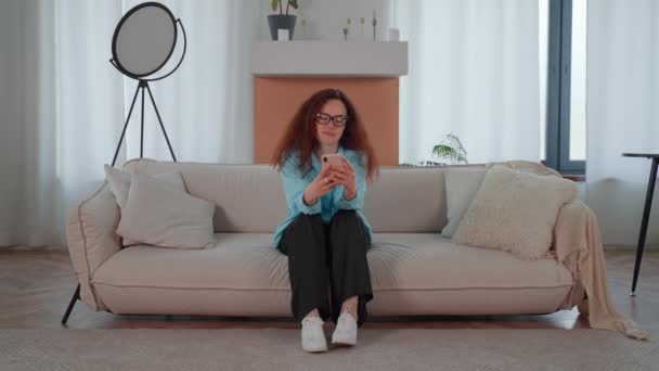 Femeie Este Așezată Canapea Înglobată Telefonul Mobil Derulează Tipărește Timp Secvență video de stoc