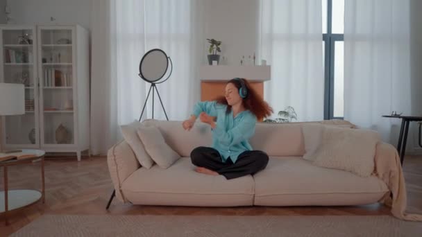 Женщина Сидит Диване Уютной Гостиной Слушая Музыку Используя Наушники Наслаждаясь — стоковое видео