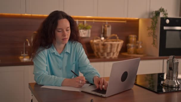 一个女人坐在厨房的柜台前 一边工作一边专注于她的笔记本电脑屏幕上 她在网上打字 写笔记 看讲座或主课 图库视频