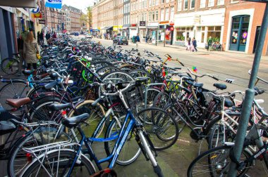 Amsterdam 'ın caddesinde belirlenmiş bir bisiklet park alanı var. Bir sıra renkli ve çeşitli bisikletler oraya park edilmiş, bazıları metal parmaklıklara yaslanmış. Bu hareketli sahne gösteriyor ki...