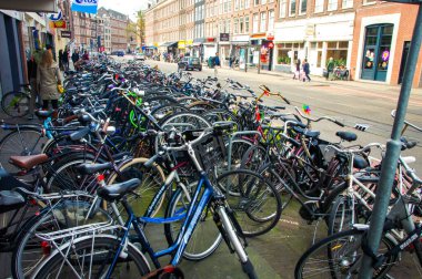 Amsterdam 'ın caddesinde belirlenmiş bir bisiklet park alanı var. Bir sıra renkli ve çeşitli bisikletler oraya park edilmiş, bazıları metal parmaklıklara yaslanmış. Bu hareketli sahne gösteriyor ki...