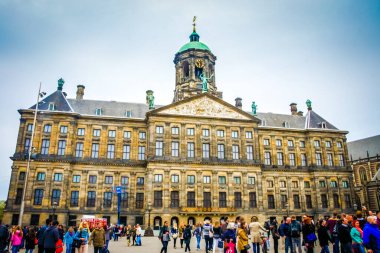 Amsterdam 'ın hareketli şehir merkezi Baraj Meydanı' nda, kırmızı tuğlalarla döşenmiş geniş bir açık alanda sergileniyor. 17. yüzyıl binaları arasında toplanan kalabalık, burayı popüler bir turizm merkezi haline getiriyor..