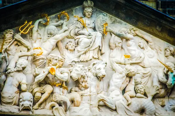 stock image A group sculptures in Amsterdam features a central figure of a woman on a building adorned with gold accents. The woman, dressed in a flowing white dress, holds a trident.