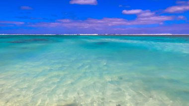 Serene turquoise lagoon stretches towards distant horizon, framed by fluffy clouds in Cook Islands, a peaceful tropical paradise. clipart