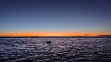 Cook Adaları gün batımı. Altın ışık, sakin sularda yansıyan gökyüzünü yıkıyor. Doğanın nefes kesici bir başyapıtı. Cook Adaları çarpıcı göksel renkler sergiliyor..