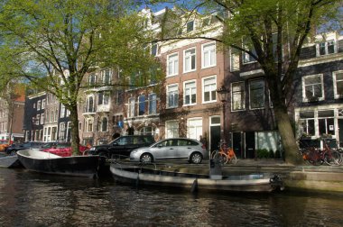Park etmiş arabalar ve teknelerle dolu sakin bir Amsterdam kanalı. Amsterdam 'da demirli teknelerle dolu bir su yolunda hareketli bir sahne. Huzurlu Amsterdam kanal ayarları. Amsterdam 'ın toplam 17. yüzyıl kanal bölgesi