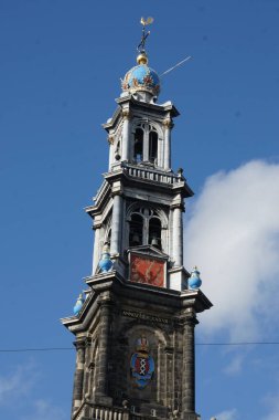 Amsterdam 'ın tarihi bir simgesi olan Westerkerk' ın üzerinde parlak mavi bir kubbe bulunan uzun, sekizgen bir saat kulesi bulunuyor. Fotoğraf, gökyüzüne doğru dramatik bir perspektiften kuleyi yakalıyor.
