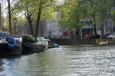 Amsterdam mı? Park etmiş tekne ve arabalarla dolu huzurlu bir kanal. Sakin sular şehri kasıp kavuruyor. Resimli bir manzara ve kanal turu için muhtemel bir rota. Alternatif olarak, manzaralı olabilir.