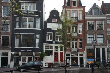 Dar, parlak renkli tarihi kanal evleri Hollanda, Amsterdam 'da bir cadde üzerindedir. Dükkanlar zemin katları işgal ediyor ve cadde boyunca manzaralı bir kanal akıyor..