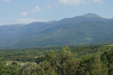 Dağ sırası, Bulgaria. Bereketli yeşil yamaçlar, berrak mavi gökyüzüne ulaşmak için yükselir. Uzak köyler aşağıdaki vadiyi işaretliyor. BÜLGARYA, doğanın ihtişamının ve kırsal sükunetin bir sembolü. Bu manzaralı manzara