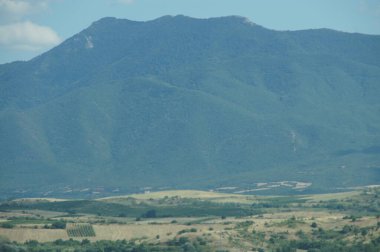 Mountain range, BULGARIA. Lush green slopes rise to a pointed peak under a bright blue sky. Rolling hills and farmland stretch into the distance. BULGARIA. Symbol of nature's grandeur and rural life. clipart