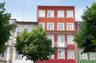 Canlı kırmızı bina, beyaz süs, balkonlar, yemyeşil ağaçlar, açık mavi gökyüzü. Braga, Portekiz. Sembol kentsel yenilenme, tarihi koruma. Şehrin mimari mirasına resimli bir bakış..