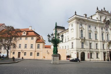 Prag 'daki Başpiskoposun Sarayı. Barok mimarisi, Başpiskoposun Sarayı 'nın gösterişli cepheleri ve büyük pencereleriyle meydana hakim. Bir sokak lambası tam ortasında duruyor.