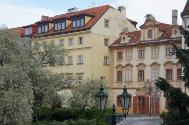 Süslü camları ve kırmızı kiremit çatıları olan renkli binalar. Önünde çiçek açan ağaçlar. Barok ve Rönesans dönemlerinden mimari detaylar. Çek Cumhuriyeti. Bu bir...